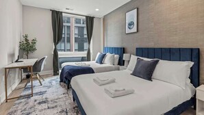 Habitación de hotel con dos camas, un escritorio, una silla, una ventana con cortinas y un cuadro colgado en la pared.