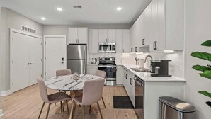 Una cocina moderna con gabinetes blancos, electrodomésticos de acero inoxidable y una mesa de comedor de mármol.