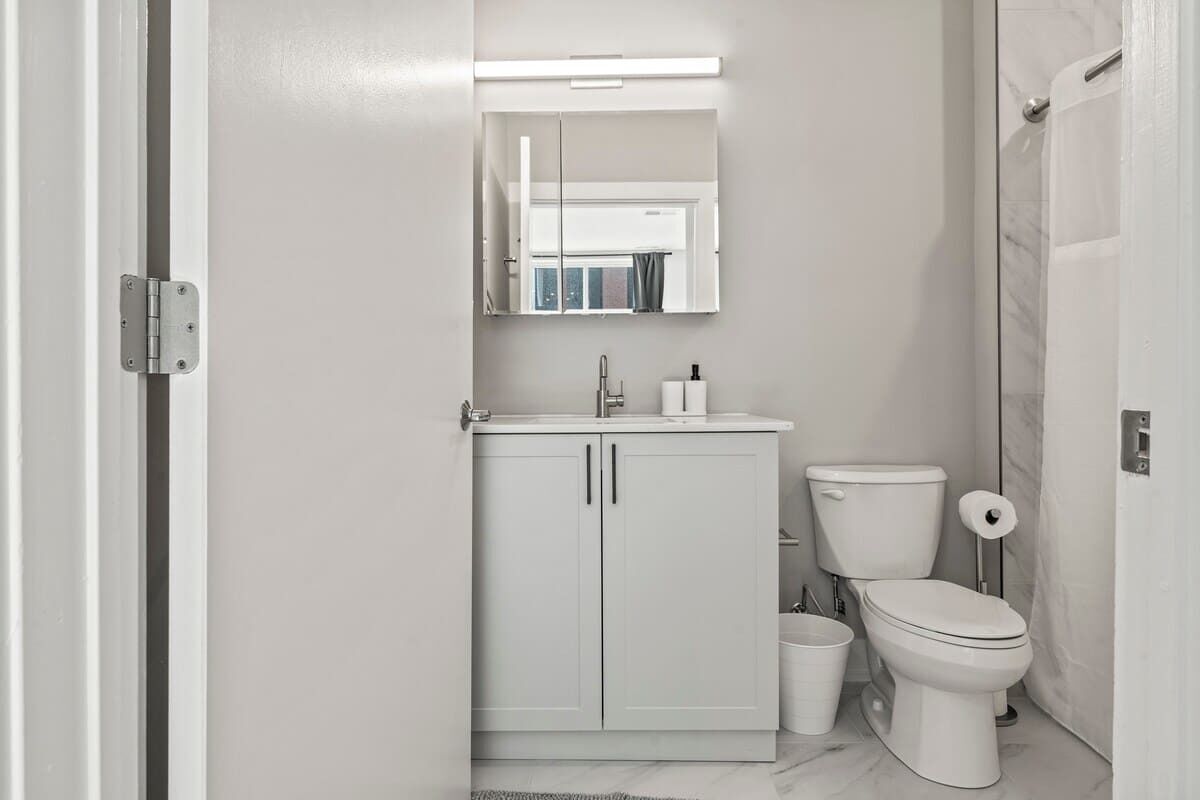 Un bagno moderno con un mobile lavabo bianco, un water e uno specchio sopra il lavandino.