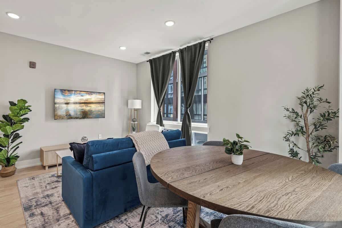 A modern living room with a blue sofa, a round wooden coffee table, and a large window with curtains.