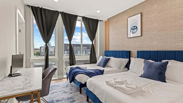 A hotel room with two beds, a desk, and a large window with curtains.
