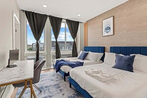 A hotel room with two beds, a desk, and a large window with curtains.