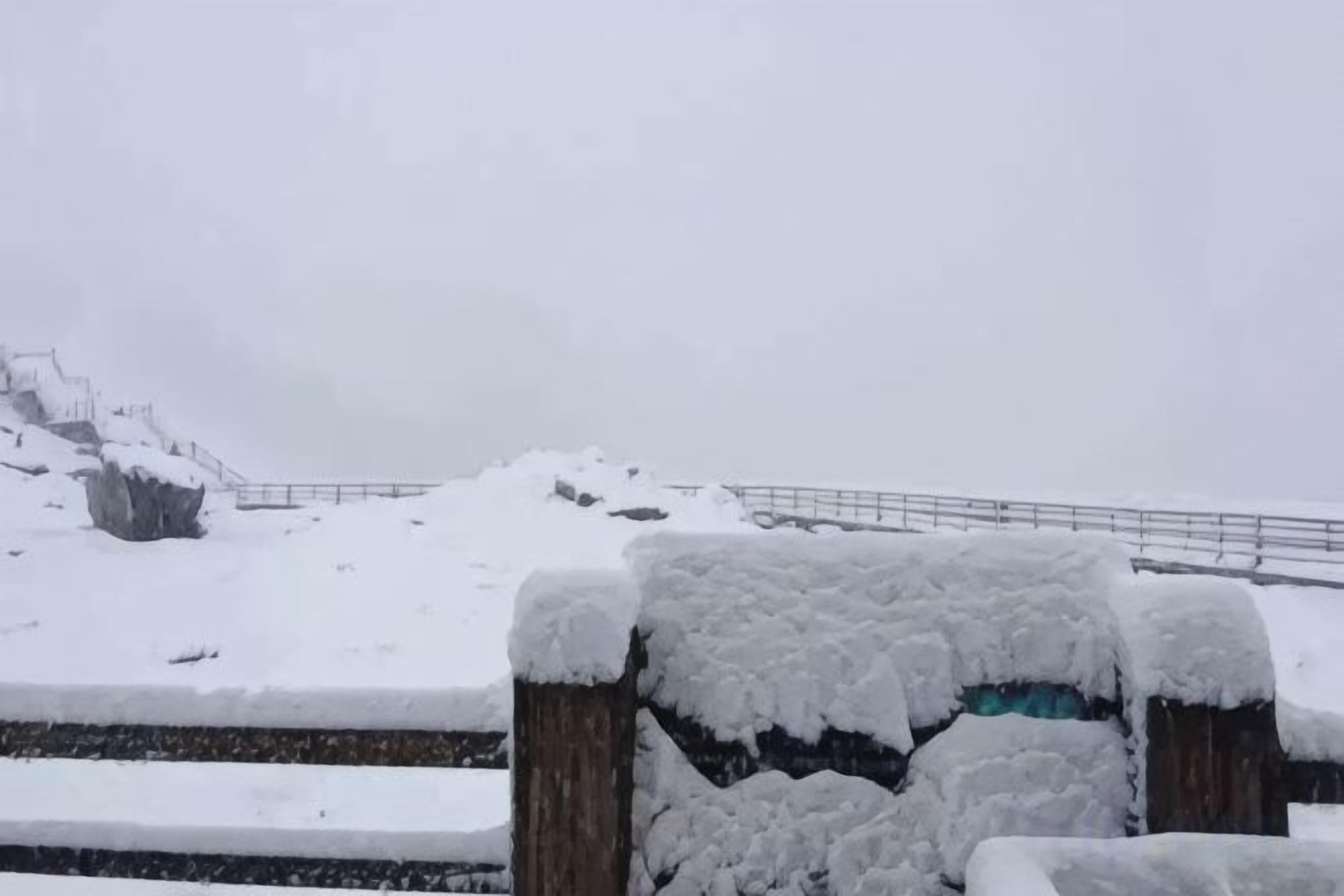 A snow-covered outdoor area with a wooden fence and a metal railing.
