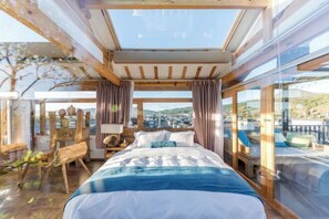 A bedroom with a large bed, wooden beams, a skylight, and a view of a town. - Jingfengtang Guest House (Lijiang)