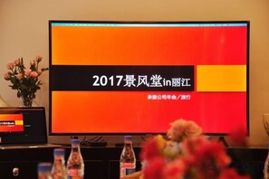 A television displaying text in a foreign language, a vase with flowers, and a water bottle on a table.