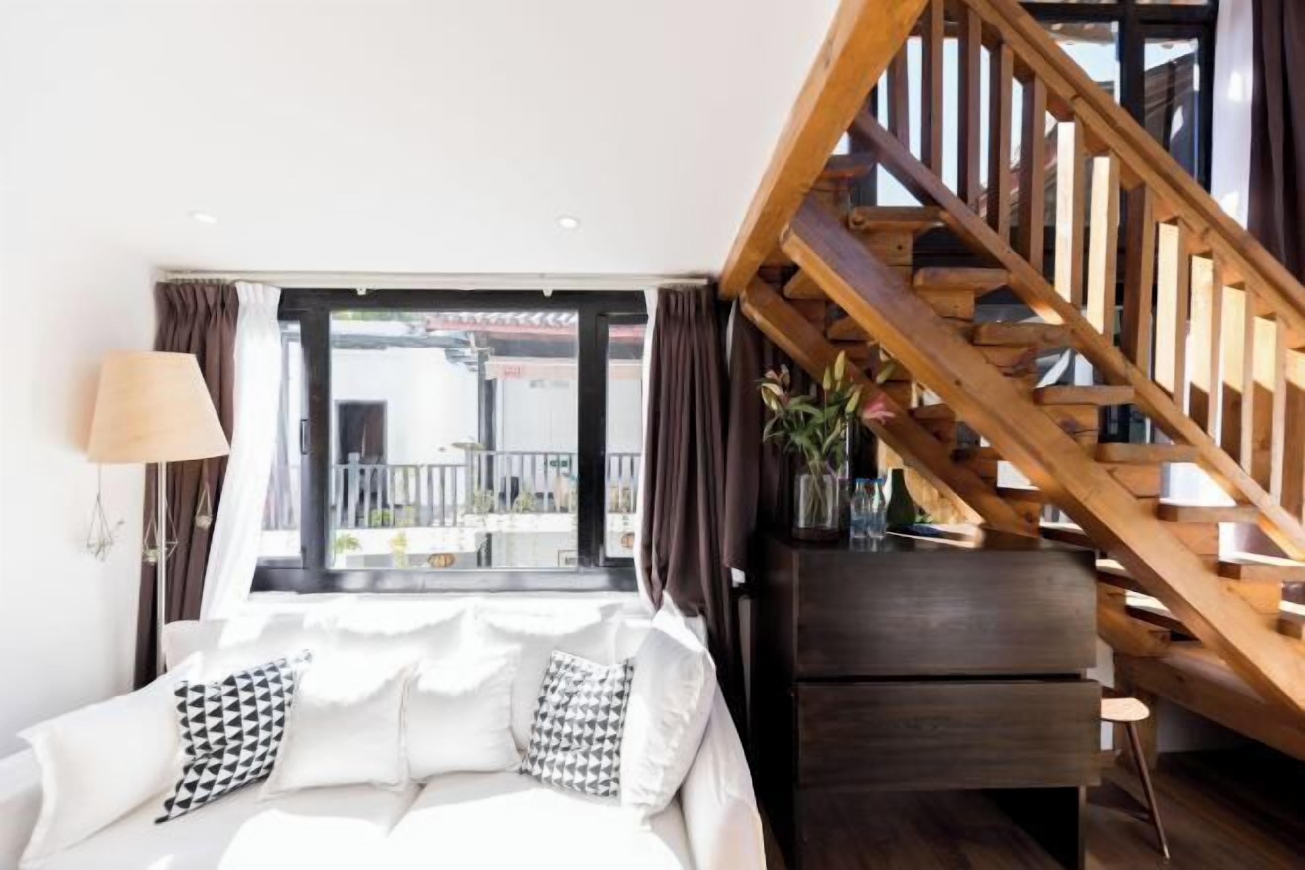 Una sala de estar moderna con un sofá blanco, una escalera de madera y vistas a través de un amplio ventanal.