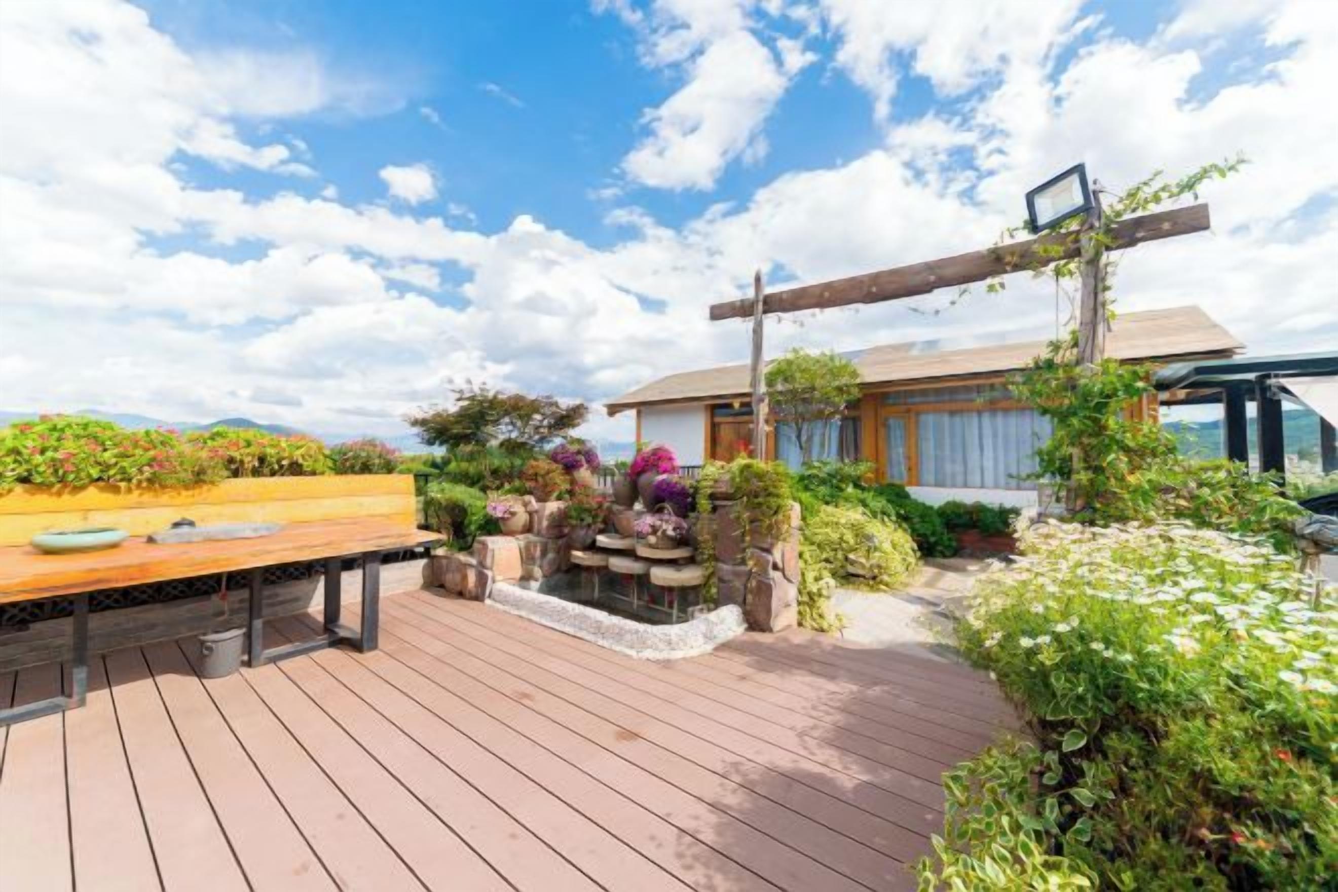 A wooden deck with a table and chairs, surrounded by lush greenery and a small water feature.