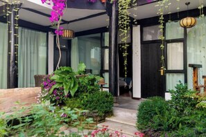 A covered outdoor area with a wooden bench, potted plants, and hanging plants. - Jingfengtang Guest House (Lijiang)