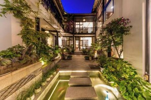 A courtyard with a water feature, potted plants, and a building with a balcony. - Jingfengtang Guest House (Lijiang)