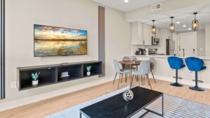 A modern living room with a large flat-screen TV, a black coffee table, and a dining area with a wooden table and chairs. - Luxury 2BD | 4 Beds | Northern Liberties (Philadelphia)