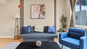 A modern living room with a grey sofa, a blue armchair, and a black coffee table with a decorative sphere. - Luxury 2BD | 4 Beds | Northern Liberties (Philadelphia)
