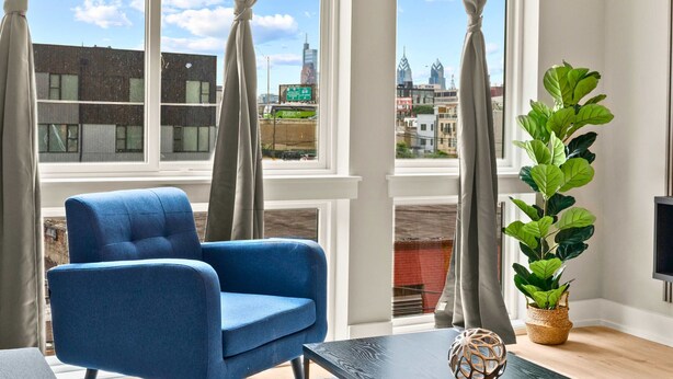A room with a large window, a blue armchair, a potted plant, and a flat-screen TV. - Luxury 2BD | 4 Beds | Northern Liberties (Philadelphia)