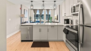 A modern kitchen with white cabinets, stainless steel appliances, and a large window with curtains. - Luxury 2BD | 4 Beds | Northern Liberties (Philadelphia)