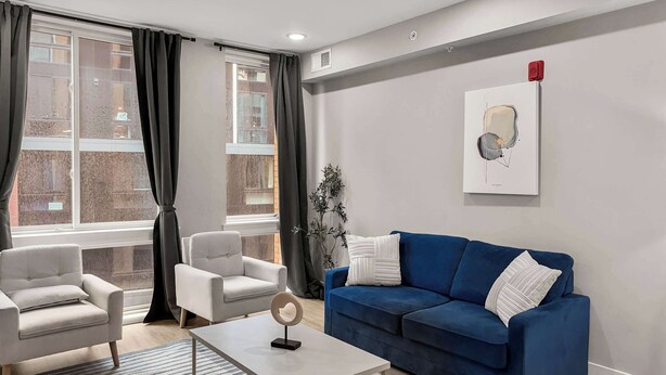A modern living room with a blue sofa, two armchairs, a coffee table, and a large window with curtains. - Luxury 1BD | 3 Beds | Northern Liberties (Philadelphia)