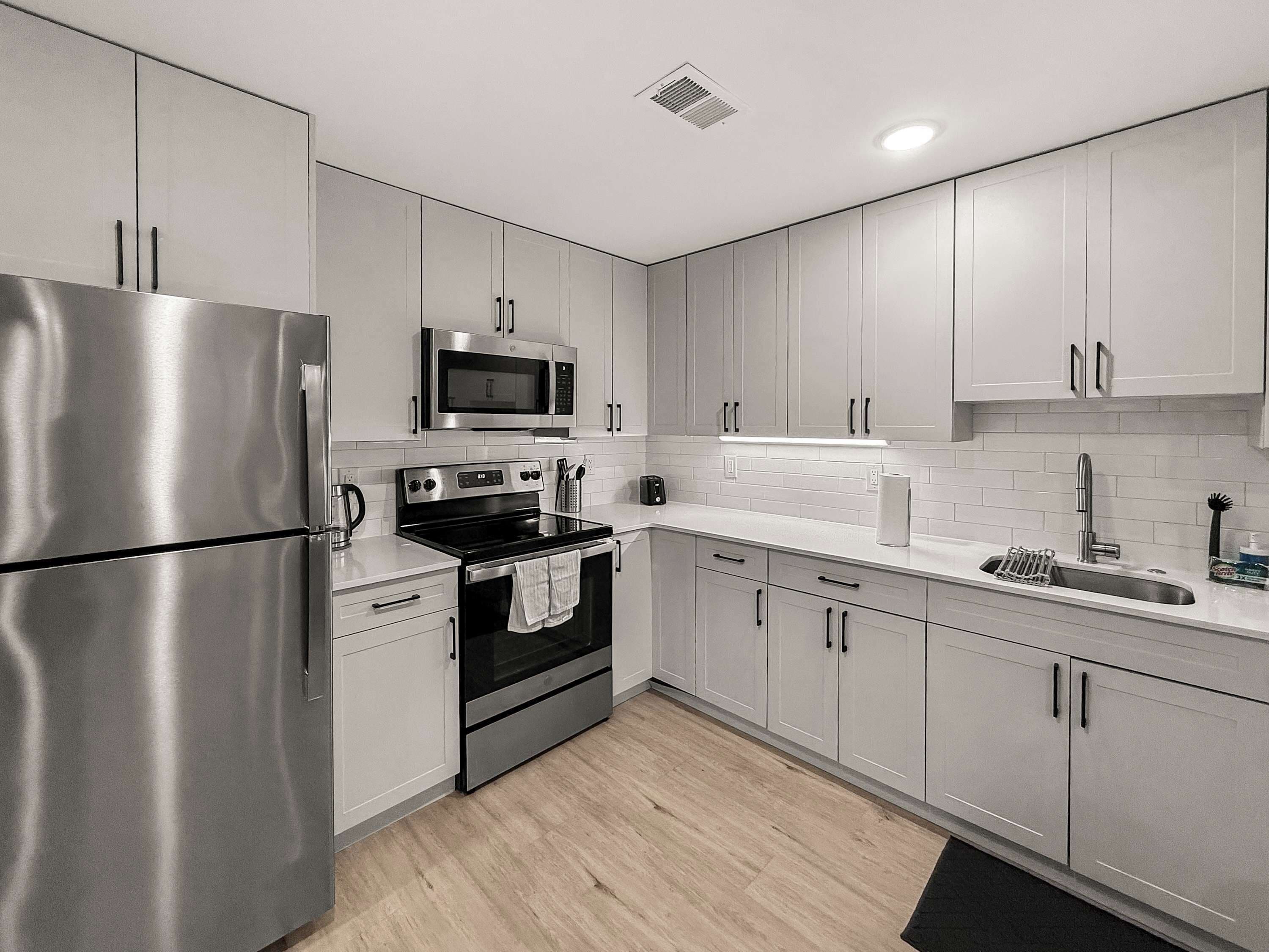 A modern kitchen with stainless steel appliances, white cabinets, and a tiled backsplash.