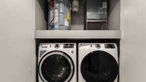 Two front-loading washing machines in a laundry room with a built-in water heater and a small shelf above them. - Luxury 1BD | 3 Beds | Northern Liberties (Philadelphia)