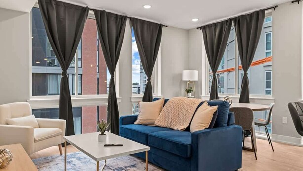 A modern living room with a blue sofa, white armchair, and a small table. - Luxury 1BD | 2 Beds | Northern Liberties (Philadelphia)