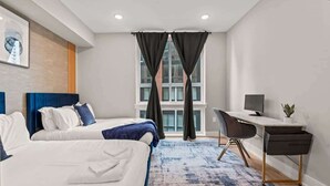 A hotel room with two beds, a desk, a chair, a TV, and a window with curtains. - Luxury 1BD | 2 Beds | Northern Liberties (Philadelphia)