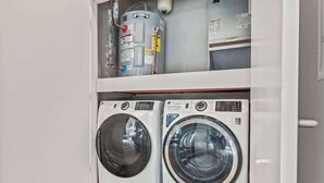 A laundry room with two front-loading washing machines and a water heater on the shelf above. - Luxury 1BD | 2 Beds | Northern Liberties (Philadelphia)