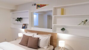 Ein ordentlich eingerichtetes Schlafzimmer mit einem Bett, Nachttischen, einem Spiegel und Regalen mit dekorativen Gegenständen.