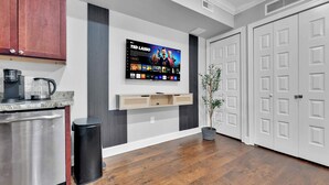 Eine moderne Küche mit Kaffeemaschine, Mülleimer und einem an der Wand montierten Fernseher, der eine Sendung zeigt.