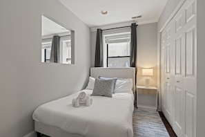 A hotel room with a bed, a nightstand, a lamp, a window with curtains, and a wardrobe.