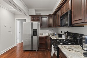 Une cuisine équipée d’un réfrigérateur en acier inoxydable, d’une cuisinière noire, de meubles en bois et d’un plan de travail en marbre.