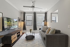 A modern living room with a flat-screen TV, a ceiling fan, a sofa, and a coffee table.