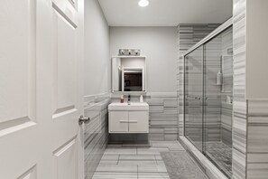 Et badeværelse med et hvidt toiletbord, en brusekabine med glaslåger og et spejl over vasken.