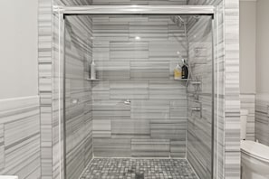 A modern bathroom with a glass-enclosed shower, marble tiles, and a toilet.