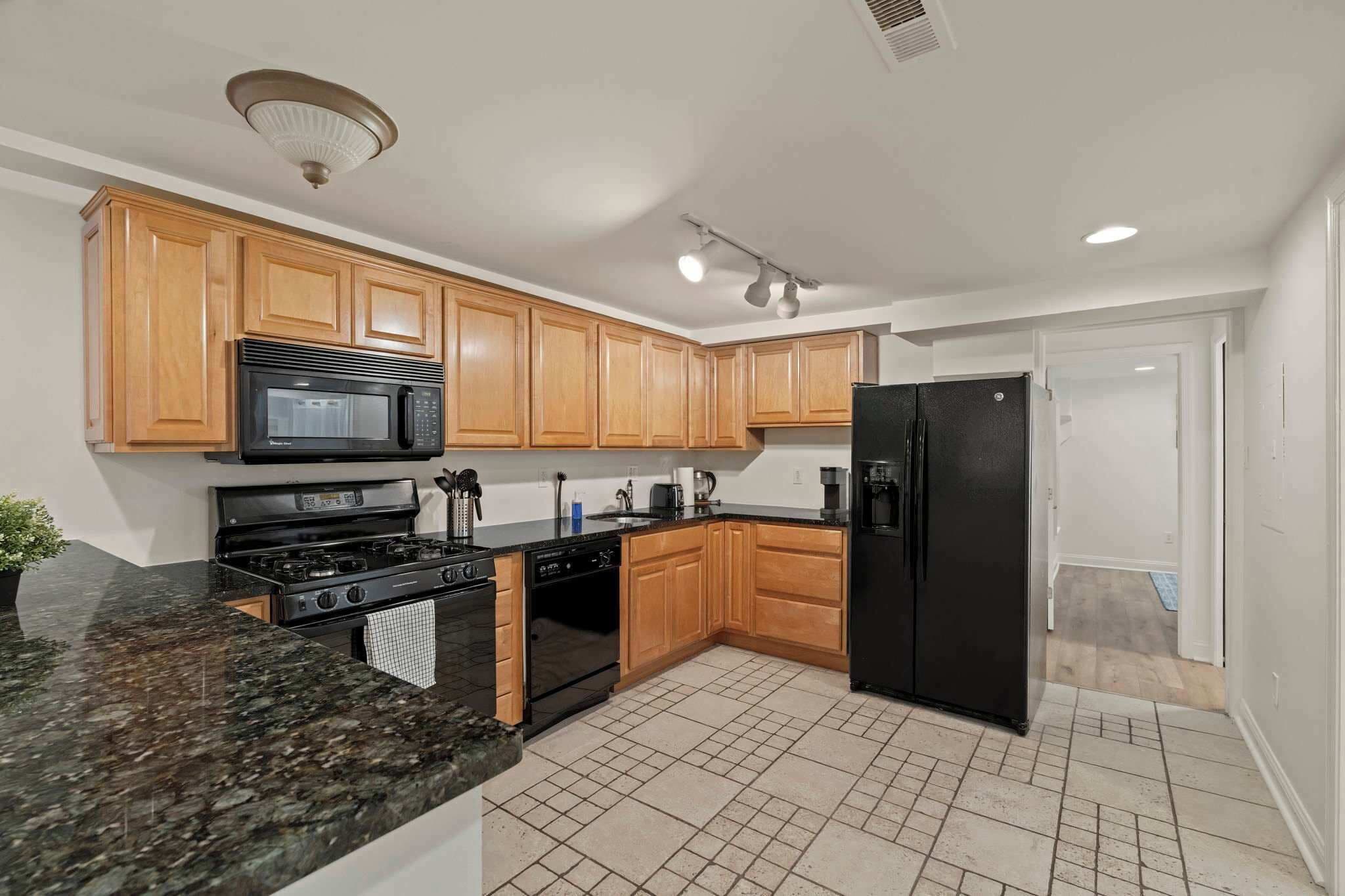 A kitchen with wooden cabinets, a black refrigerator, a microwave, a stove, and a dishwasher.