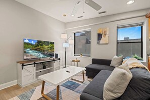 A modern living room with a flat-screen TV, a sofa, a coffee table, and a window with blinds.
