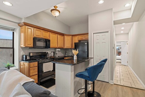 A modern kitchen with wooden cabinets, a black refrigerator, a stove, and a bar stool.