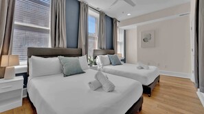 A hotel room with two beds, a nightstand, a lamp, and a window with curtains.