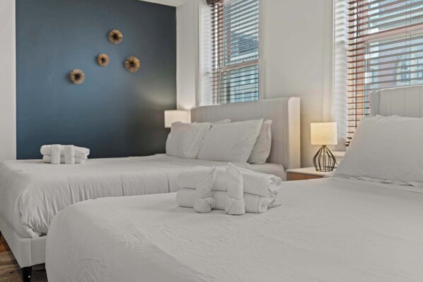 Habitación de hotel con dos camas, una pared de acento azul y una ventana con persianas.