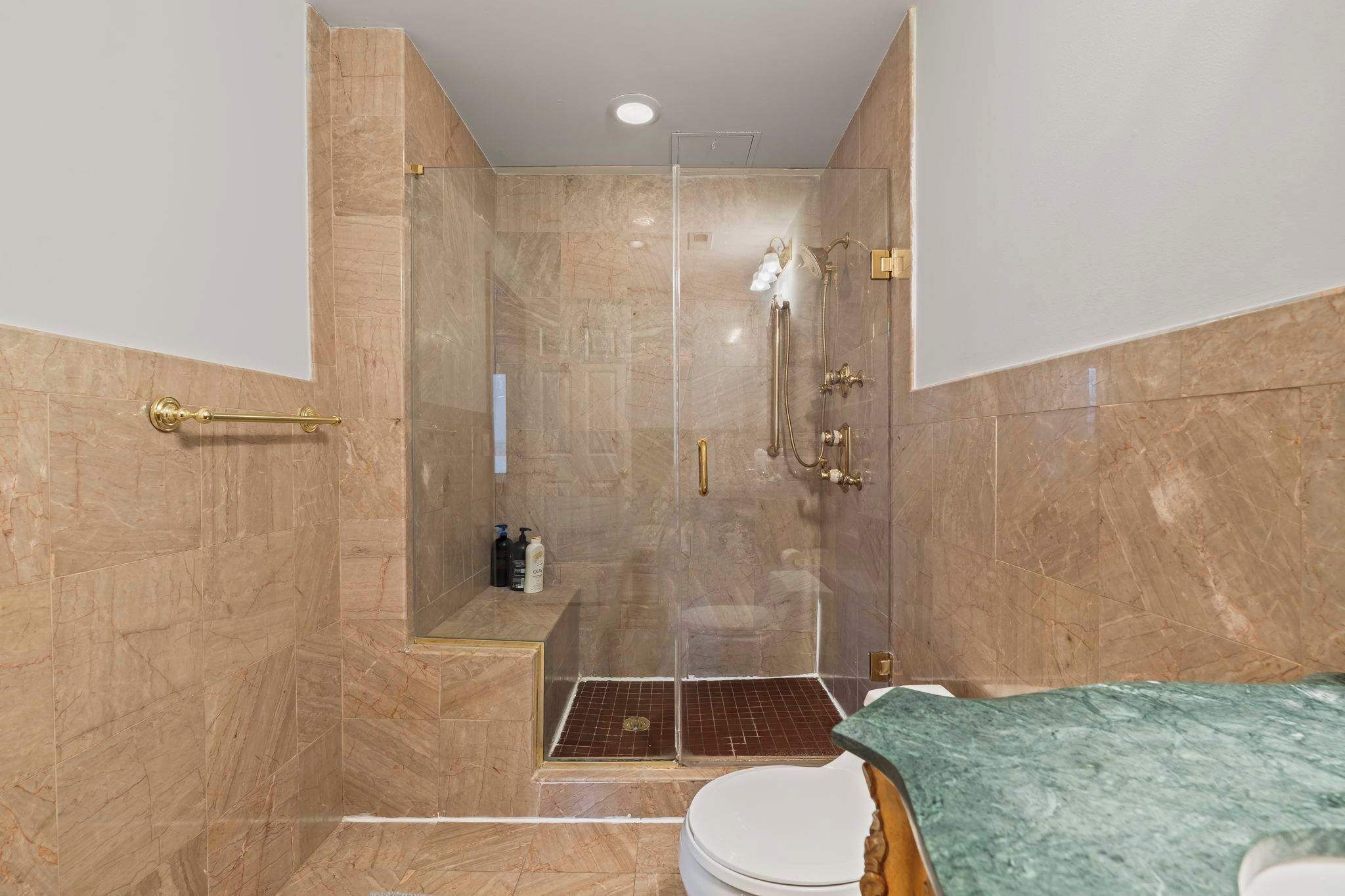 A bathroom with a glass-enclosed shower, a toilet, and a sink with a green countertop.