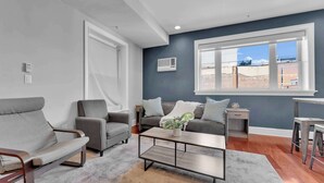 Ein modernes Wohnzimmer mit grauem Sofa, Sesseln, einem Couchtisch und einem großen Fenster mit Blick auf Gebäude.