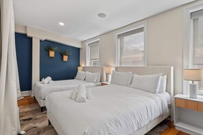 A hotel room with two beds, a blue accent wall, and a large window.
