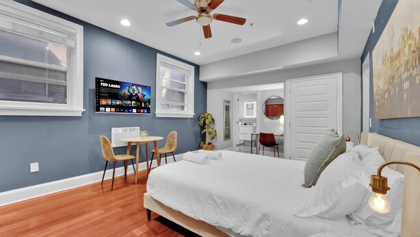 A bedroom with a bed, a desk, two chairs, a ceiling fan, and a TV on the wall. - Cozy Studio | Old City | 1Bed |Independence Hall (Philadelphia)