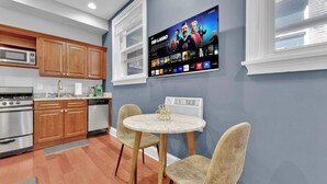 A modern kitchen with wooden cabinets, a stainless steel stove, and a wall-mounted flat-screen TV displaying a streaming service interface. - Cozy Studio | Old City | 1Bed |Independence Hall (Philadelphia)