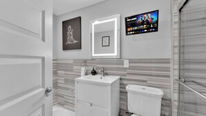 A modern bathroom with a vanity, toilet, and a TV mounted on the wall displaying a show. - Cozy Studio | Old City | 1Bed |Independence Hall (Philadelphia)