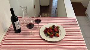 Une table à manger recouverte d’une nappe à rayures, deux chaises blanches, une bouteille de vin, deux verres à vin et une assiette de fraises.