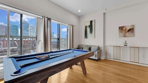Una mesa de billar en una habitación con ventanas amplias, un sofá y un cuadro en la pared.