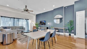 A modern living room with a sofa, coffee table, dining table, chairs, a TV, and a ceiling fan.