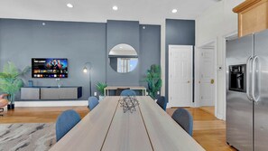 A modern kitchen with a built-in refrigerator, a dining table with chairs, a TV mounted on the wall, and a mirror above the table.
