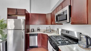A modern kitchen with stainless steel appliances, wooden cabinets, and a marble countertop. - Bright 1BR Retreat | Sleeps 4 | by Liberty Bell (Philadelphia)