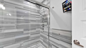 A modern bathroom with a glass shower enclosure, a digital screen displaying media content, and a sleek door handle.