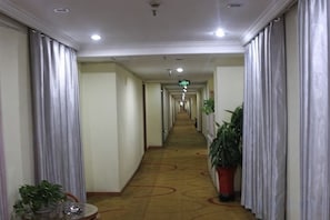Ein Hotelkorridor mit Teppichboden, Türen auf beiden Seiten und Blumentöpfen.