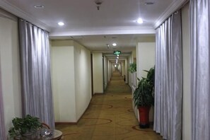 Ein Hotelgang mit Teppichboden, Vorhängen an beiden Seiten und Topfpflanzen.