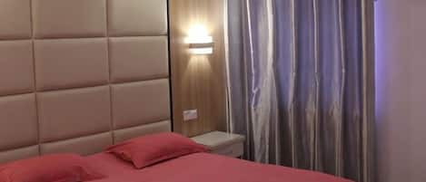 A hotel room with a bed, a nightstand, a wall-mounted light, and a curtain.
